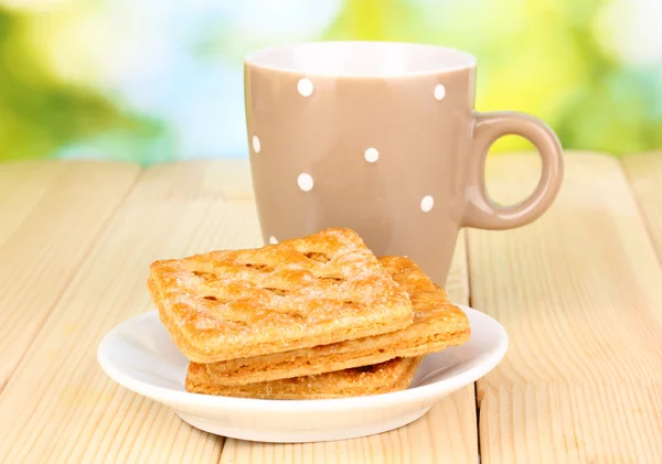 Taza de té y galletas sobre mesa de madera sobre fondo brillante — Foto de Stock