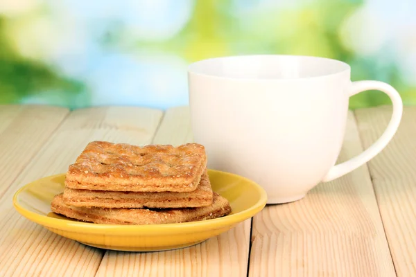 Taza de té y galletas sobre mesa de madera sobre fondo brillante — Foto de Stock