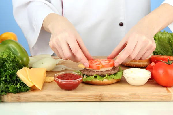 Female hands preparing cheeseburger, on blue background — Stock Photo, Image