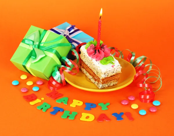 Colorful birthday cake with candle and gifts on orange background — Stock Photo, Image