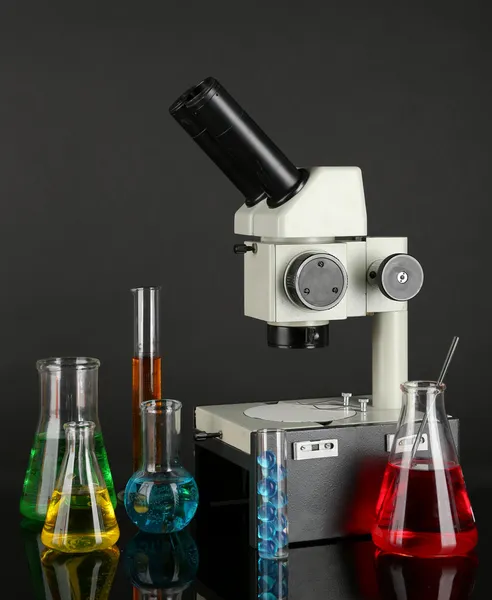 Test tubes with colorful liquids and microscope on dark grey background — Stock Photo, Image