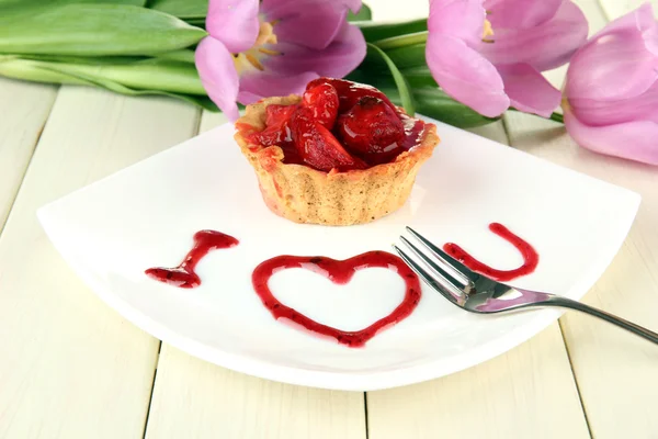 Söt tårta med jordgubbar och sås på plattan, på trä bakgrund — Stockfoto