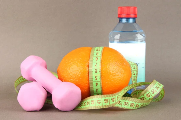 Oranje met het meten van tape, halters en fles water, op een achtergrond met kleur — Stockfoto