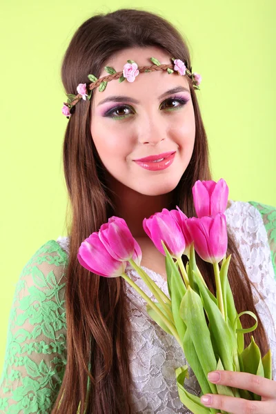 Junges schönes Mädchen mit dekorativem Kranz auf dem Kopf mit Blumenstrauß auf grünem Hintergrund — Stockfoto