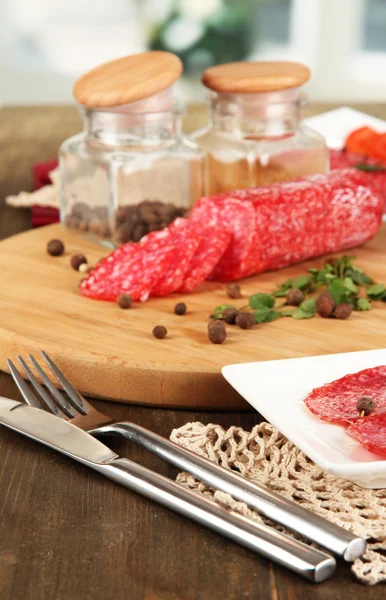 Välsmakande salami på plattan och styrelsen på träbord på fönsterbakgrund — Stockfoto