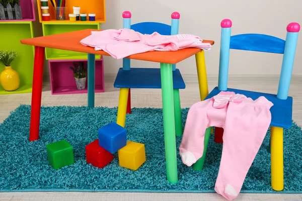 Small and colorful table and chairs with baby clothes — Stock Photo, Image