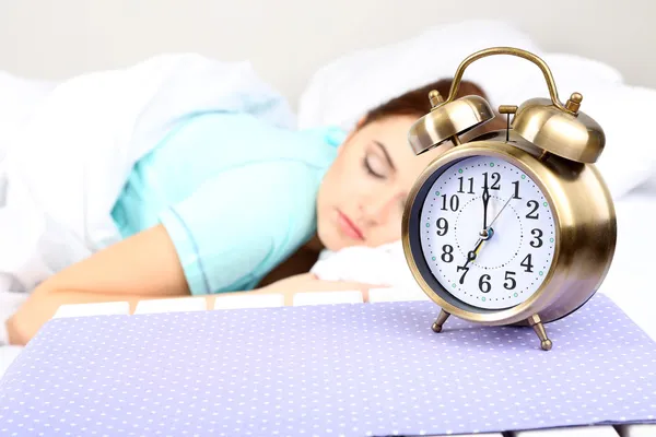 Beautiful young woman sleeping on bed with alarm clock in bedroom — Stock Photo, Image