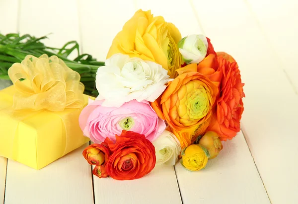 Ranunculus (persian buttercups) and gift, on white wooden background — Stock Photo, Image