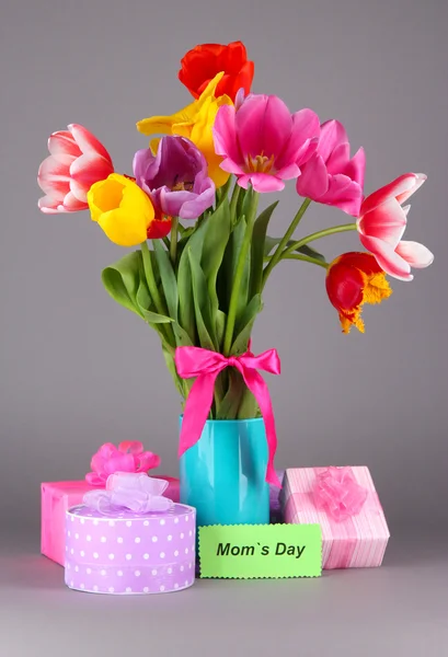 Beautiful tulips in bouquet with gifts and note on gray background — Stock Photo, Image