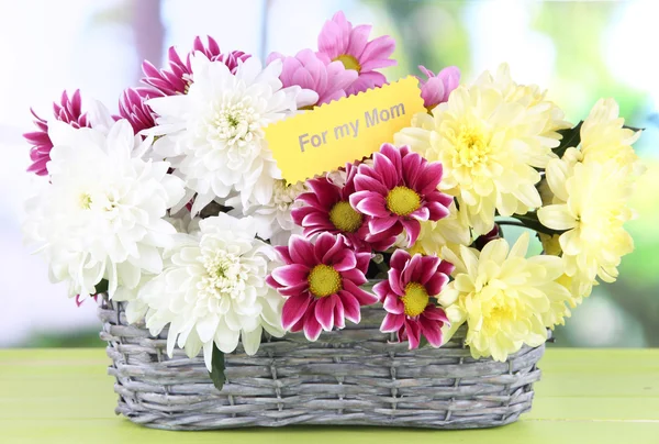 Bouquet of beautiful chrysanthemums in wicker basket on table on bright background — Stock Photo, Image