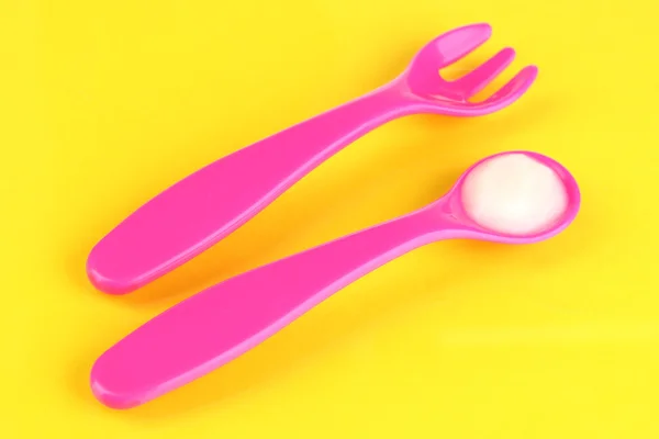 Cucchiaio rosa e forchetta per alimenti per bambini su sfondo giallo — Foto Stock