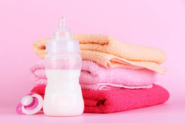 Botella para leche con toallas y pezón sobre fondo rosa —  Fotos de Stock