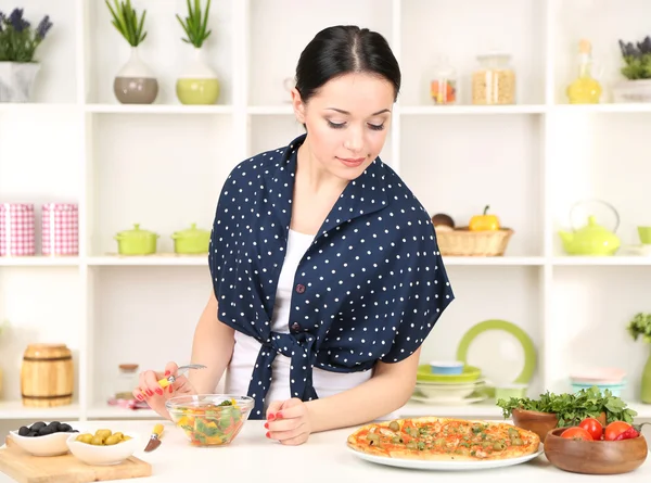 Красивая девушка выбирает пиццу или диету на фоне кухни — стоковое фото