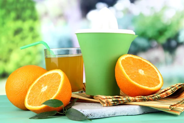 Citrus press, glass of juice and ripe oranges on green wooden table — Stock Photo, Image