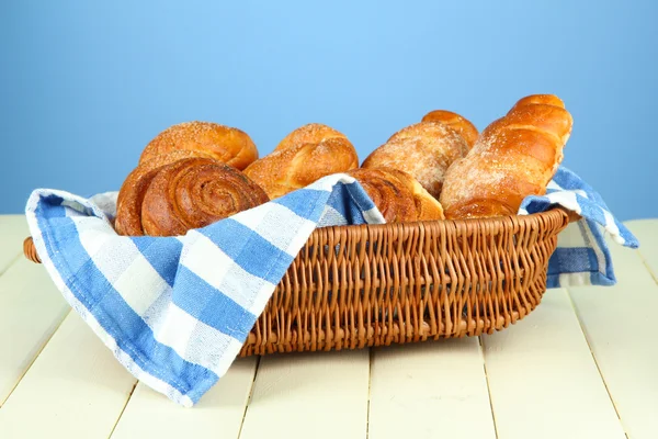 Composition with buns in wicker basket, on wooden table, on color background — Stock Photo, Image