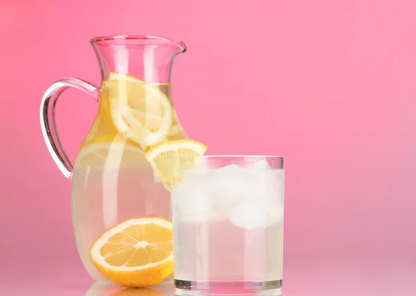 Lemonade in pitcher and glass on red background — Stock Photo, Image