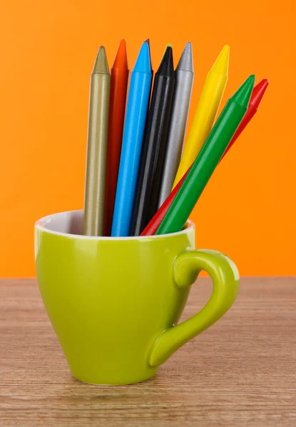 Buntstifte in Tasse auf Tisch auf orangefarbenem Hintergrund — Stockfoto