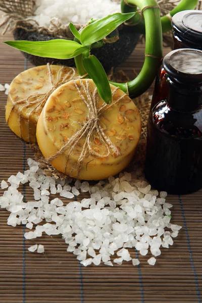 Sapone fatto a mano, bottiglie e sale marino su tappetino grigio di bambù — Foto Stock