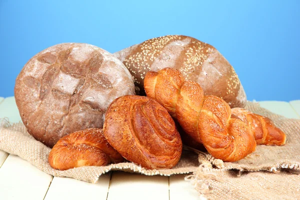 Samenstelling met brood, broodjes op rouwgewaad, op houten tafel, op een achtergrond met kleur — Stockfoto