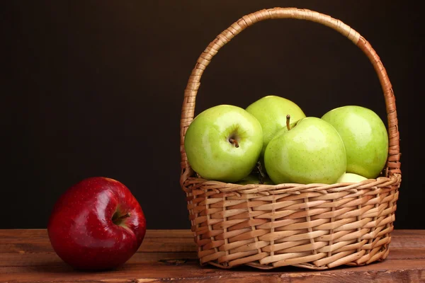 Manzanas verdes jugosas en cesta y manzana roja sobre mesa de madera sobre fondo marrón —  Fotos de Stock