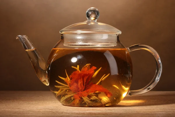 Скляний чайник з екзотичним зеленим чаєм на дерев'яному столі на коричневому фоні — стокове фото