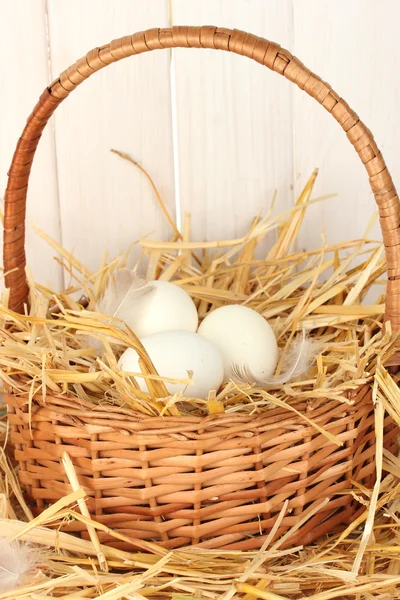 Uova bianche in un cesto di vimini su paglia su fondo di legno bianco — Foto Stock