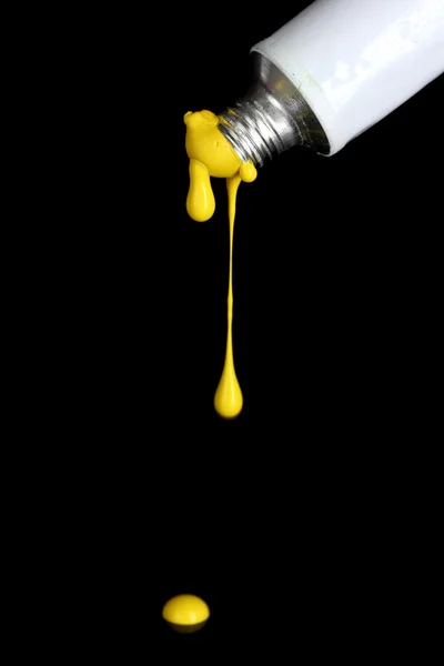 Yellow paint follows from the tube on black background close-up — Stock Photo, Image