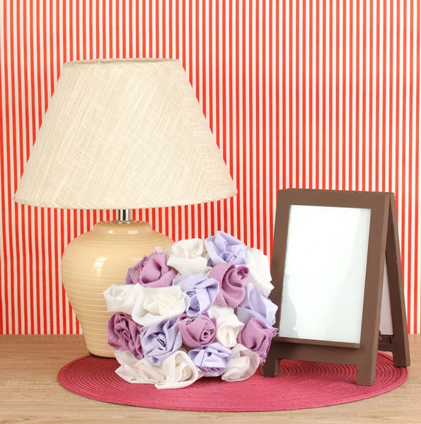 Moldura de foto marrom e lâmpada na mesa de madeira no fundo da parede listrada vermelha — Fotografia de Stock