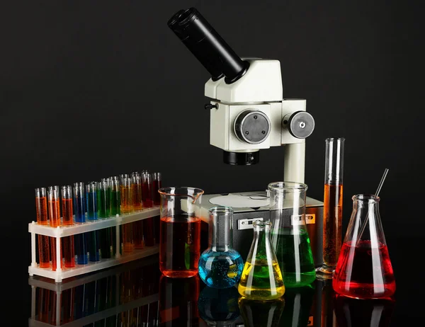 Test tubes with colorful liquids and microscope on dark grey background — Stock Photo, Image