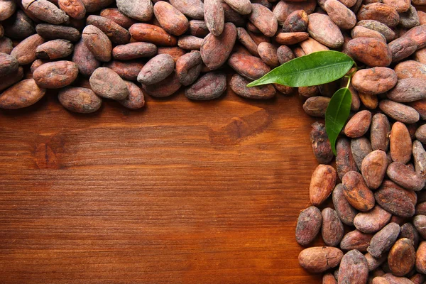 Какао бобы с листьями на деревянном фоне — стоковое фото