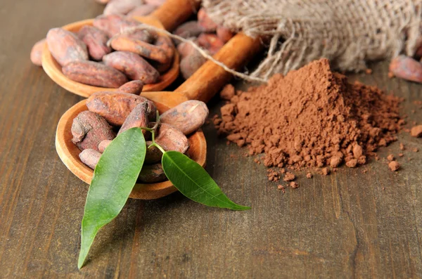 Granos de cacao en cucharas y cacao en polvo sobre fondo de madera — Foto de Stock