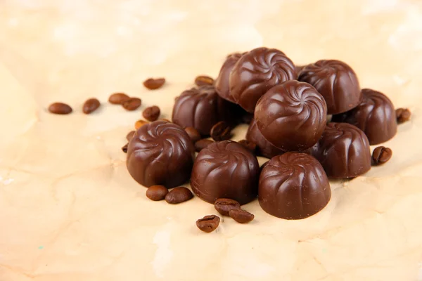 Chocolate candies and coffee beans, on beige paper background — Stock Photo, Image