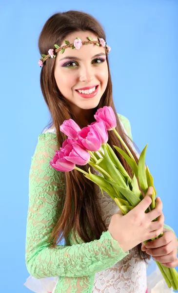 Mooi meisje met decoratieve krans op haar hoofd houden boeket van bloemen, op blauwe achtergrond — Stockfoto