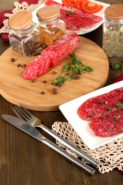 Välsmakande salami på plattan och styrelsen på träbord närbild — Stockfoto