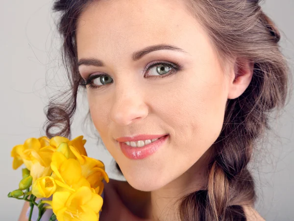 Giovane donna con bella acconciatura e fiori, su sfondo grigio — Foto Stock