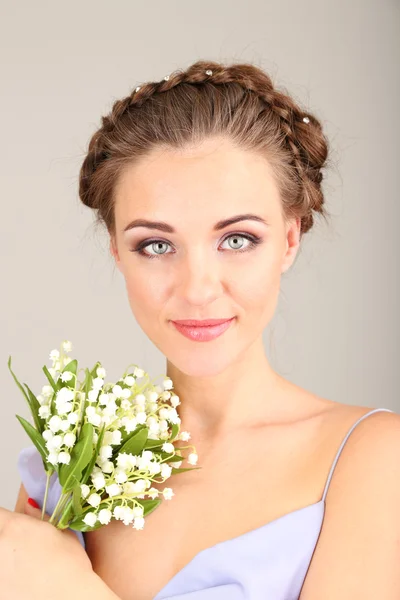 Mujer joven con hermoso peinado y flores, sobre fondo gris — Foto de Stock