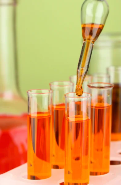 Pipeta de laboratorio con gota de líquido de color sobre tubos de ensayo de vidrio, primer plano — Foto de Stock