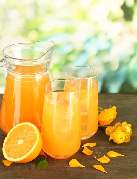 Copos e jarro de suco de laranja na mesa de madeira, no fundo verde — Fotografia de Stock