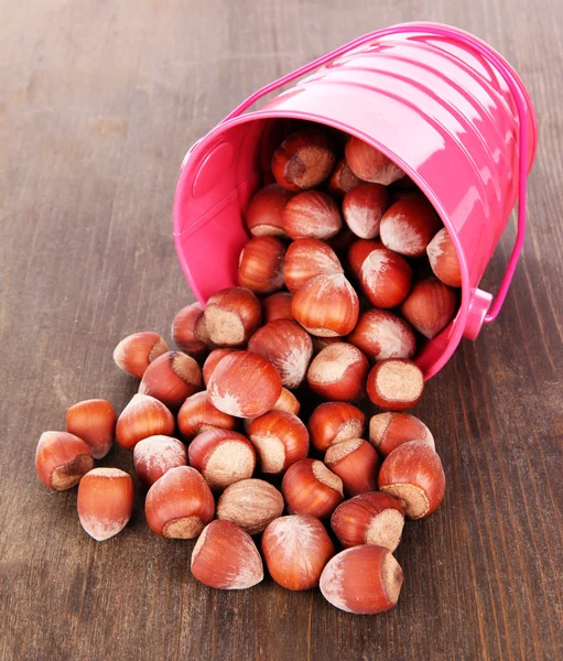 Gekanteld emmer met hazelnoten op houten achtergrond — Stockfoto