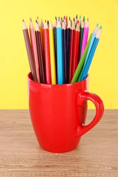 Lápis coloridos na xícara na mesa no fundo amarelo — Fotografia de Stock
