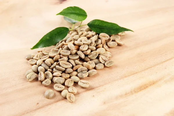 Groene koffiebonen en bladeren op houten achtergrond — Stockfoto