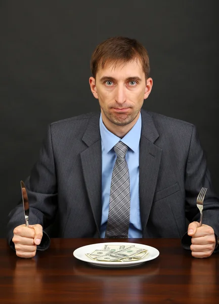 Jovem empresário jantando dólares em fundo preto — Fotografia de Stock