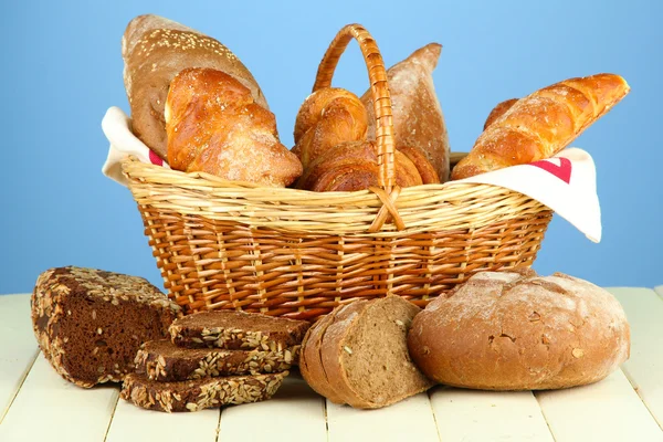 Composition with bread and rolls, in wicker basket on wooden table, on color background — Stock Photo, Image