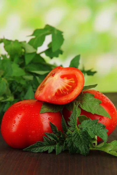 Fresh tomatoes and young plant on wooden table on natural background — Stock Photo, Image