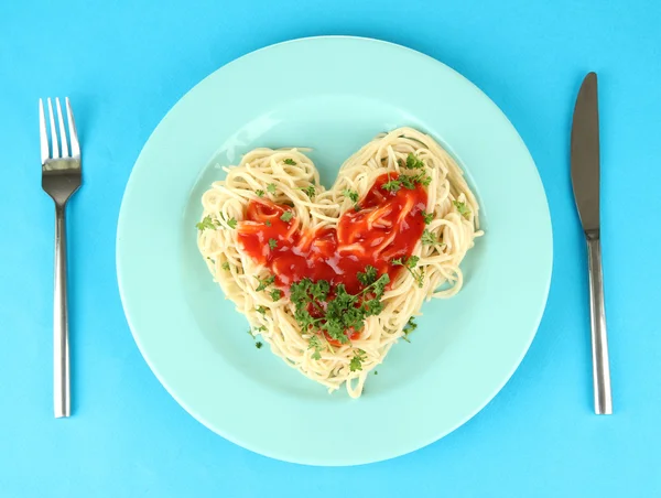 Spaghettis cuits soigneusement disposés en forme de coeur et garnis de sauce tomate, sur fond de couleur — Photo