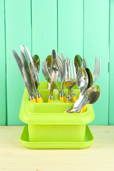 Cuchillos, cucharas, tenedores en recipiente de plástico para secar, sobre fondo de madera de color —  Fotos de Stock