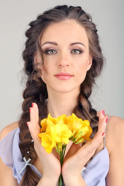 Mujer joven con hermoso peinado y flores, sobre fondo gris — Foto de Stock