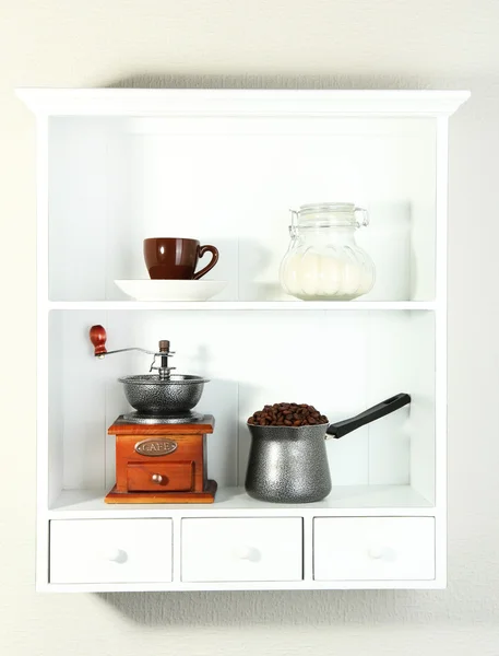 Molino de café y cafetera, taza y frasco de vidrio con azúcar en estantes blancos —  Fotos de Stock