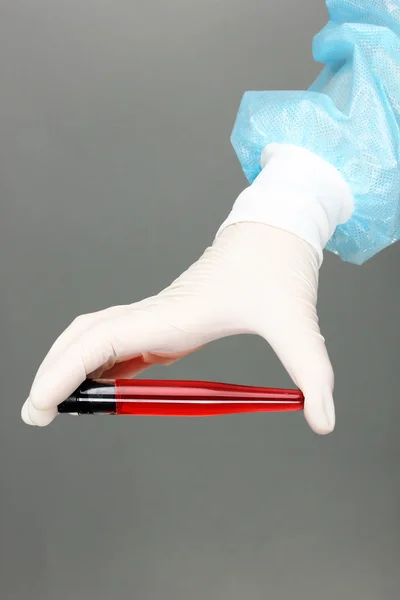 Glasröhre mit Flüssigkeit in der Hand des Wissenschaftlers während eines medizinischen Tests auf grauem Hintergrund — Stockfoto