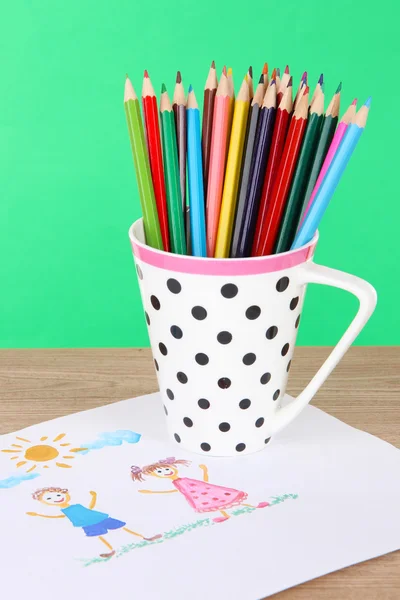 Lápis coloridos na xícara na mesa sobre fundo verde — Fotografia de Stock